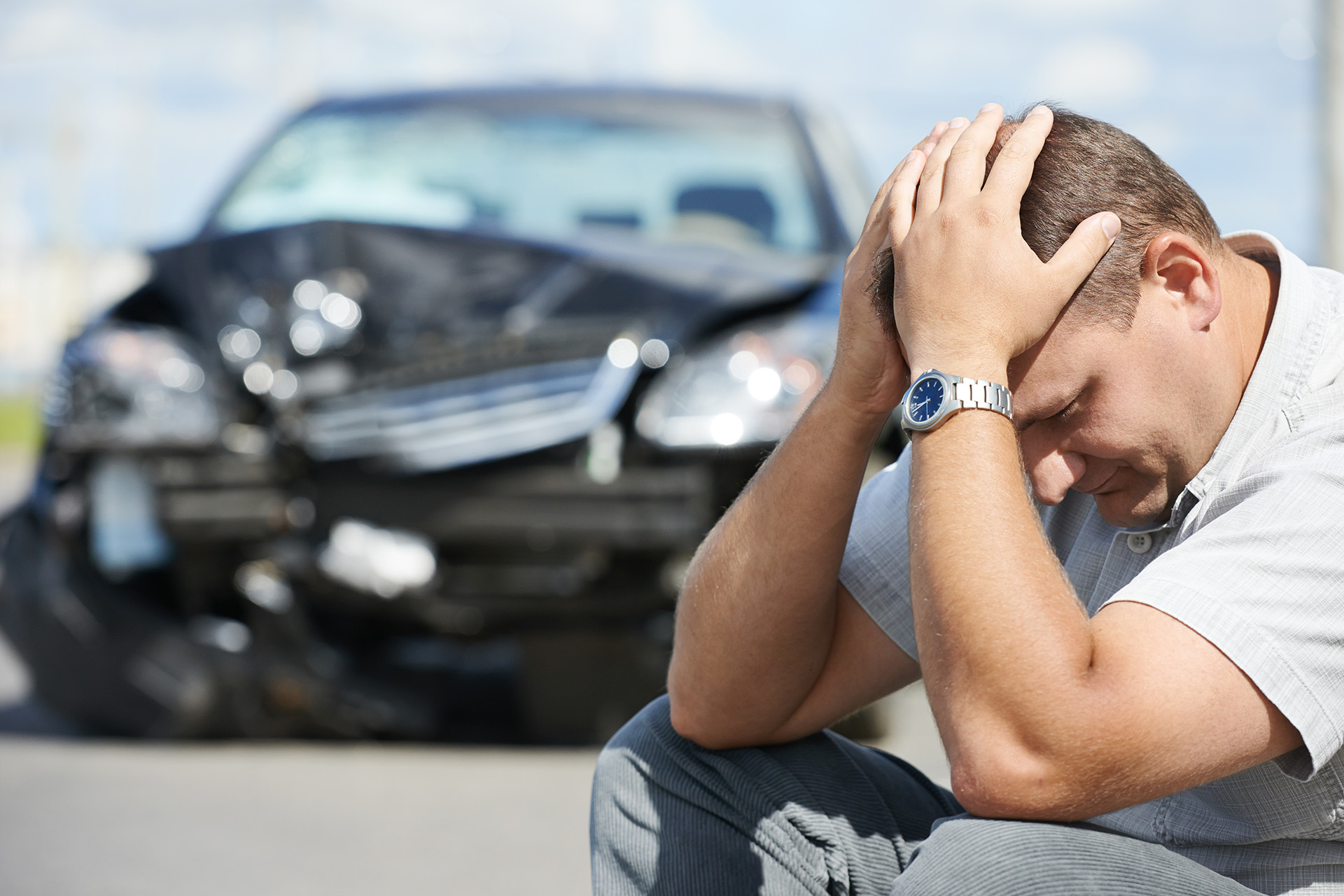 Black Automobile Damaged With Driver Sitting Outside Holding Head